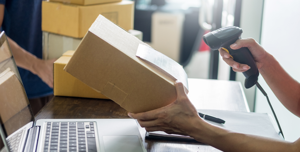 A person holds a box in one hand and a scanner in the other to illustrate the returns process